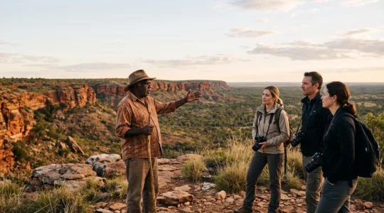 An Aboriginal cultural guide standing on ancestral land at sunrise, sharing knowledge with a small group of attentive travelers