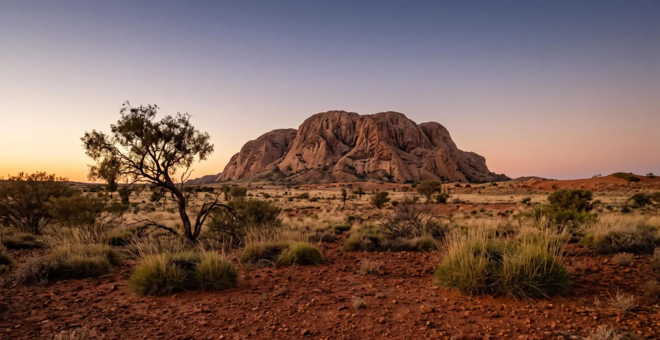 Vast ochre desert landscape at golden hour with a weathered monolithic rock formation, symbolizing an ancient landscape that functions as a living legal and ancestral record