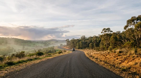 A winding coastal road cutting through Australia's diverse seasonal landscapes at golden hour, symbolizing year-round trip planning