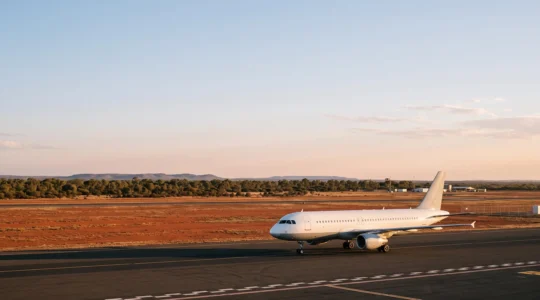 Wide aerial view of a domestic jet taxiing at an Australian airport at golden hour with red outback terrain in the distance