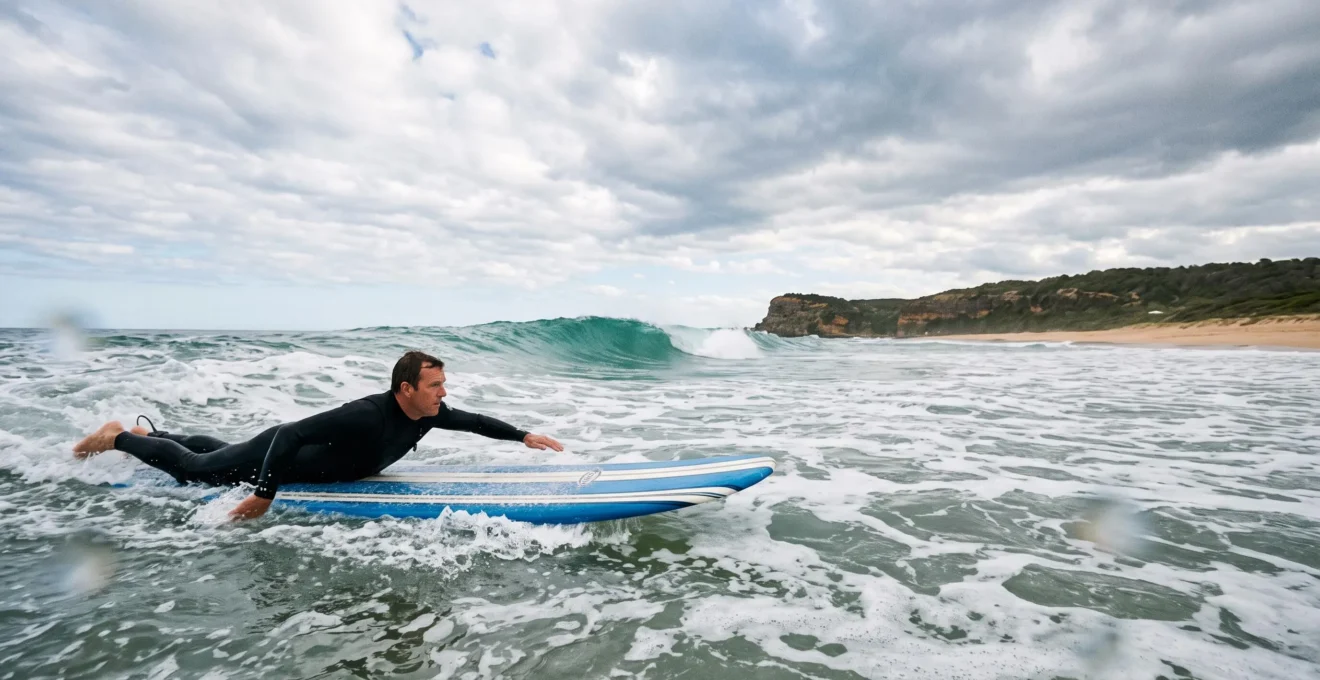 A surfer paddling from calm whitewater toward a rolling green wave under an open Australian sky, symbolizing progression from beginner to intermediate skill.