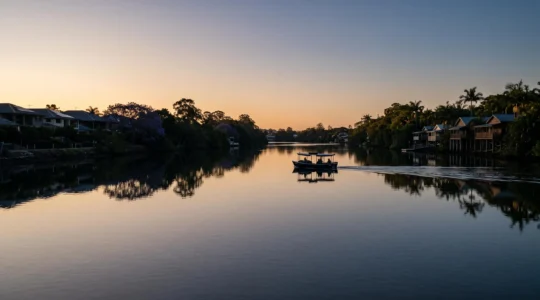 Wide dusk view of the Brisbane River curving between two riverbanks lined with subtropical trees and low-rise architecture, symbolizing the city's north-south divide and outdoor way of life