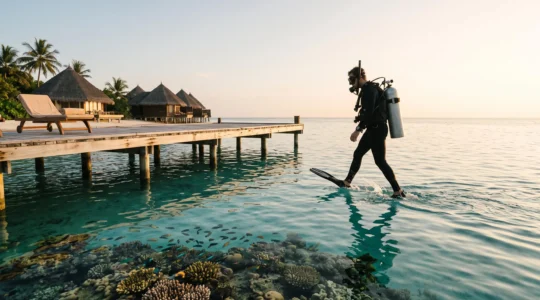 A diver descending from a small boat toward a vivid coral bommie beside a tropical island resort at sunrise, symbolizing the choice between beach leisure and serious reef access.