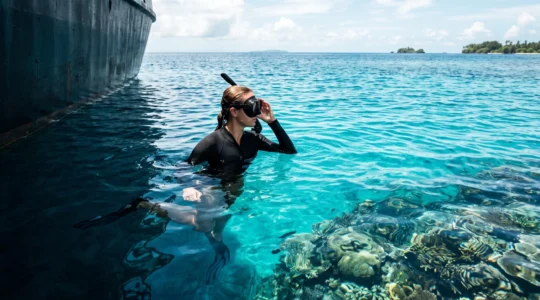 A snorkeler pausing at the surface between a boat's shadow and the open, sunlit reef, symbolizing the choice between simple transport and a guided marine encounter.