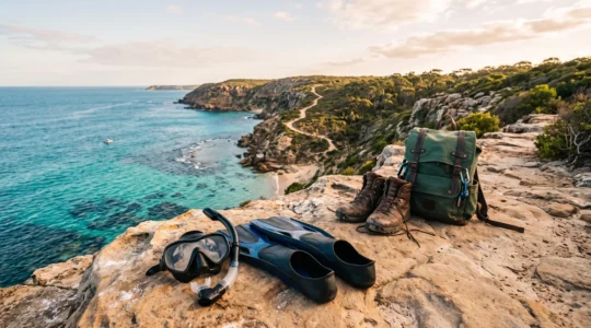 A diver's fins and a hiker's boots resting side by side on a rocky Australian coastline overlooking a coral reef at golden hour