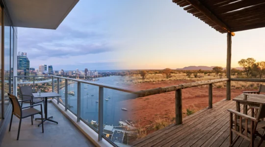 A wide editorial composition contrasting a modern city hotel balcony with a remote outback lodge deck under an Australian sky, symbolizing the choice between accommodation styles.