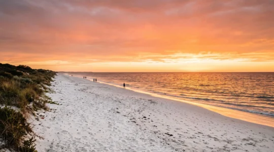 Wide golden-hour view of a nearly empty Perth beach with turquoise Indian Ocean water and dramatic sunset sky